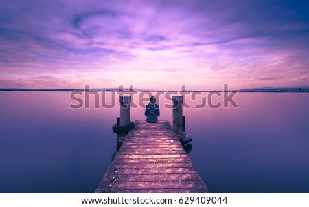 Self reflection in magical world of fantasy. One woman sits on a wooden pier. Cloudy above the lake. Long exposure Royalty-Free Stock Photo #629409044