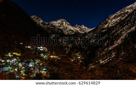 Nightscape of small village at the foothills of snow capped Himalayan mountain under moonlight and star