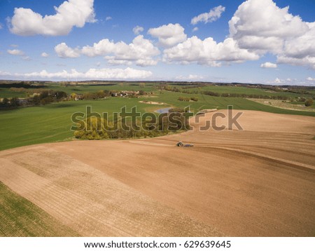 Aerial view of beautiful agricultural fields in spring with a tractor at work - tractor cultivating a field