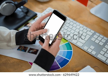 Close-up of female graphic designer using mobile phone at desk in office