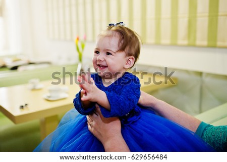 Cute little baby girl at blue dress at hands of mother.
