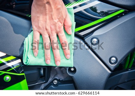 Hand with man cleaning motorcycle with green microfiber cloth 
