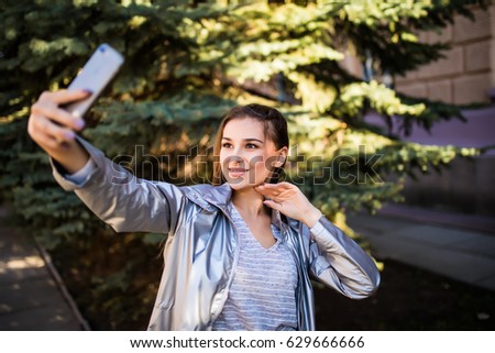 Portrait of beautiful girl in destination city street using a smart phone to take selfies pictures, sunny outdoors.