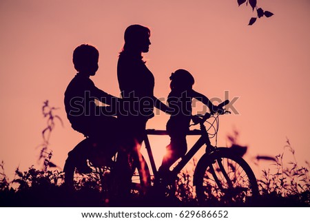 mother with son and daughter riding bike at sunset