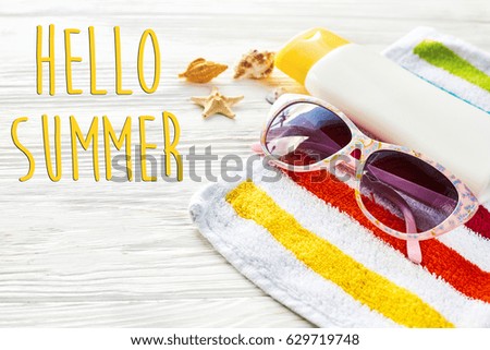 hello summer text on colorful towel, sunglasses, yellow sunscreen and star shells on white rustic wooden background, top view. space for text. travel and summer holiday at beach, vacation concept