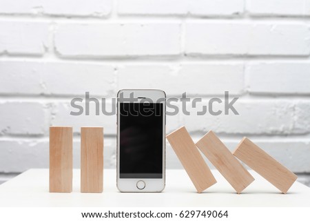 Smart phone helps business and stop the Domino principle. Business concept. On a white wooden background. Horizontally.