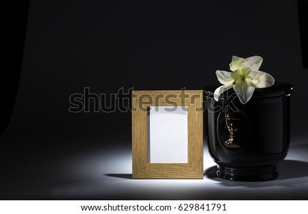 Black evangelical urn with blank mourning frame, and flower on dark background
