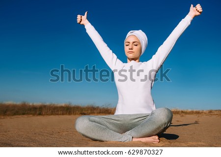 On a sunny afternoon in the sand a girl in white clothes is sitting and practicing yoga, relaxation, kundalini
 Royalty-Free Stock Photo #629870327