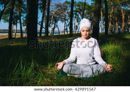 In a pine forest in summer, the girl sits in a lotus pose in white clothes and is practicing yoga kundalini closed eyes, relaxation
 Royalty-Free Stock Photo #629891567