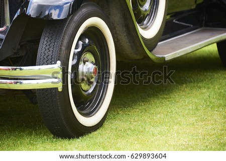 Vintage wheel of classic car on green grass lawn. Beautiful photo of a stunning retro car. Stylish vehicle. Nostalgia of past time. Close up. 