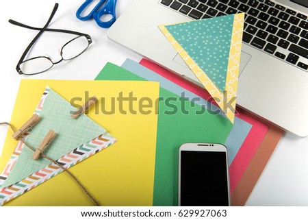 craft materials on desk including scissors and construction paper with glasses cell phone laptop