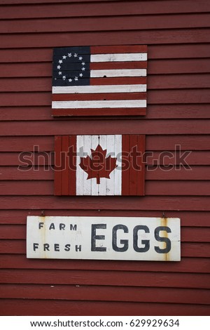 Dark red clapboard wall with wooden Betsy Ross and Canadian flag and farm fresh eggs sign