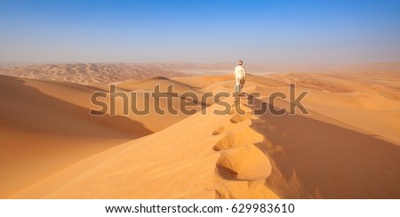 Omani Man walking over sand dune in the empty quarter Royalty-Free Stock Photo #629983610