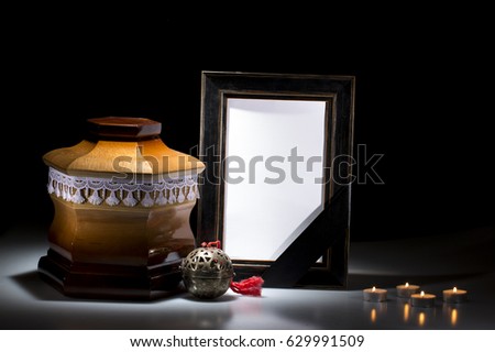 Wooden cemetery urn with black mourning frame and flower, and candles on dark background