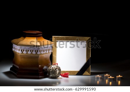 Wooden cemetery urn with blank mourning frame and flower and candles  on dark background