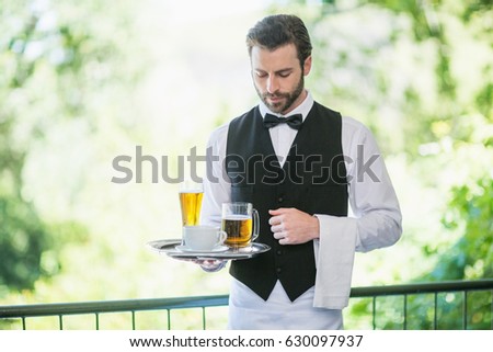 Male waiter holding tray with beer glass and coffee cup in restaurant