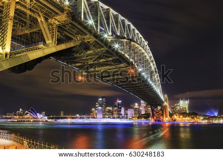 Architectural landmarks of Sydney at dark during light show. Arch of Harbour Bridge above the head towards city CBD and Circular quay. Royalty-Free Stock Photo #630248183