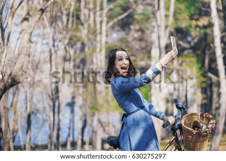 Trendy young woman stop to riding on her vintage bike with basket of flowers while focused chatting or talk on smart phone outside,gorgeous female using mobile phone during recreation time in the park