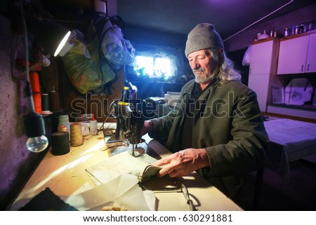 A senior adult man sewing a piece of cloth on a sewing machine.