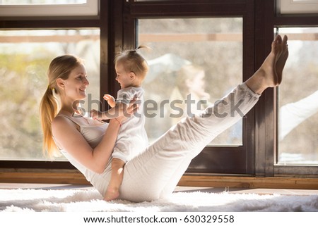 Young yogi smiling mother working out engaging her playful child, toning abs muscles, , integrating baby into yoga practice, fitness at home when having no time for gym. Healthy lifestyle concept  Royalty-Free Stock Photo #630329558
