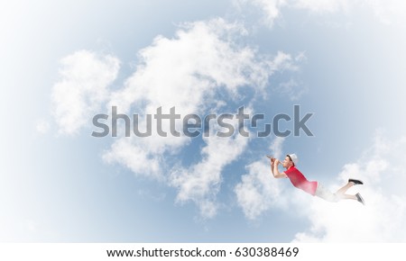 Young cheerful man flying high in sky and playing fife