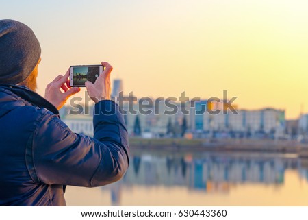 Young man in hat takes pictures of the city's panorama on a smartphone. City travel concept