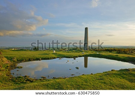 Reflections of an abandoned chimney stack from the Craddock Moor mine at twilight with sheep grazing on Bodmin Moor, Cornwall, England, UK