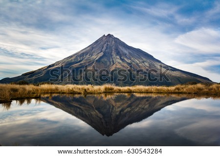 A symmetric picture of the taranaki volcano in the north island of new zealand and with the reflection of tho mountain and the climber in a lake