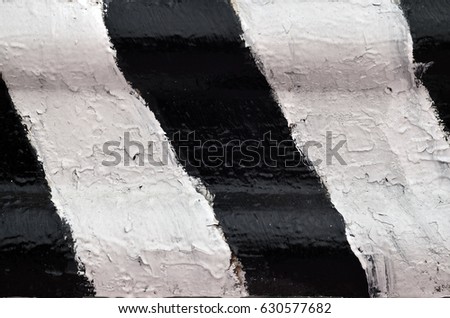 Close-up view of a metal barrier with striped color. An image of a hazard warning barrier that has been painted by hand in black and white colors