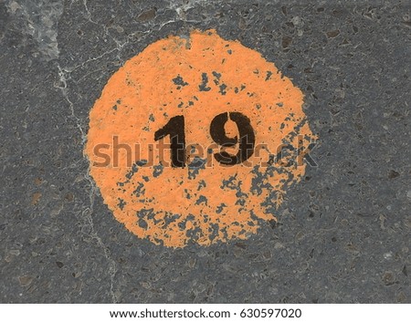 Black number 19 in an orange faded circle on concrete background.