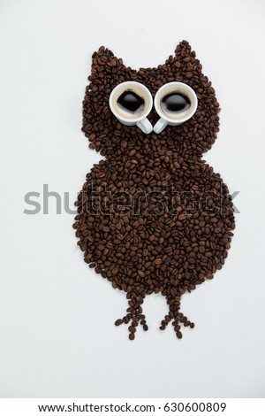 Coffee beans and cups forming owl on white background