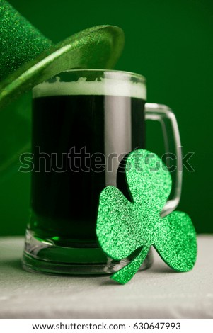 St Patricks Day leprechaun hat with mug of green beer and shamrock against green background