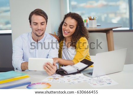 Smiling graphic designers sitting at table and using digital tablet in office