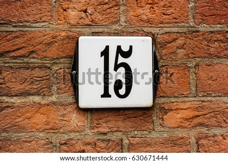 Enameled house number fifteen (15) on a red brick wall
