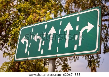 Green road intersection arrow sign with directions for five lanes on a sky and trees background stock image.
