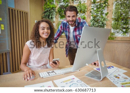 Portrait of executives smiling at desk while working on personal computer in office