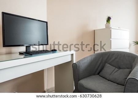 Modern office or home interior with workplace. PC workstation with wide screen and gray arm chair. Minimalist room interior in daylight. 