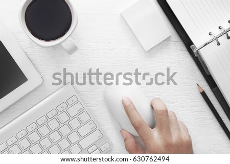 Hand holding a computer mouse Coffee mug on the table with a notebook, keyboard, computer mouse, pencil