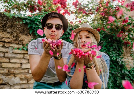 Young lovely couple blowing rose petals at the camera. The hipster couple are wearing hats and just sharing some love.
