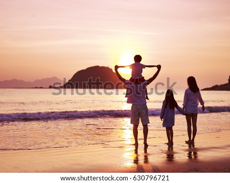 asian family standing on beach watching and enjoying the sunrise.