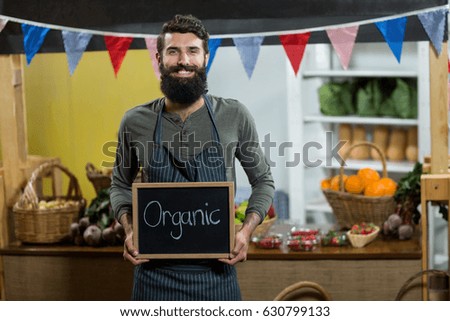 Portrait of a worker holding a board with organic sign at grocery store