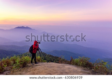 red coat photographer with tripod shoot landscapre picture on top of mountain with blue and purple sky in the evening