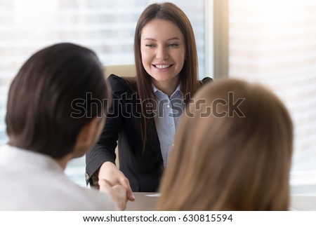 Attractive cheerful businesswoman and couple shaking hands over a desk closing real estate deal or partnership, finishing up or starting meeting, estate agent and client handshaking at office