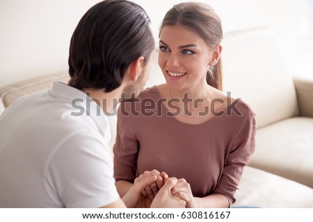 Portrait of beautiful excited woman looking at her boyfriend with affection while he proposing to marry, young man holding ladyâ??s hands declaring his feelings, saying I love you, marriage proposal