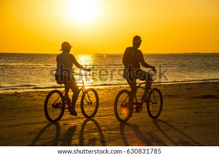 Couple rides bicycles in sunset rays on Sanibel Island. Royalty-Free Stock Photo #630831785