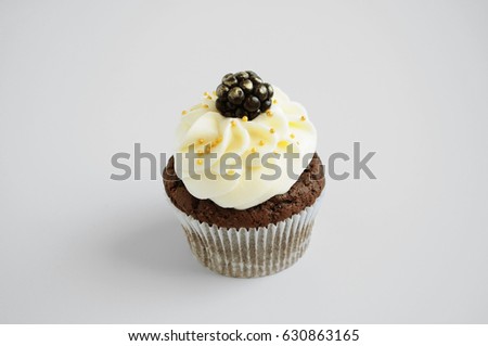 Chocolate cupcake with white cream, blackberry and gold confectionery sprinkling. Isolated. Picture for a menu or a confectionery catalog.