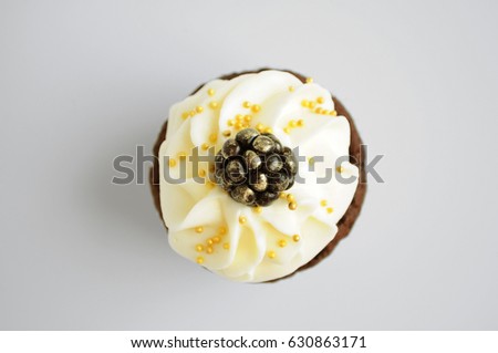 Chocolate cupcake with white cream, blackberry and gold confectionery sprinkling. Isolated. Top view. Picture for a menu or a confectionery catalog.