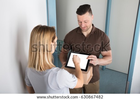 View Of A Young Woman Signing After Receiving Box From Delivery Man 