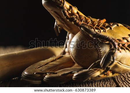 Close up image of an old used baseball, baseball bat, and baseball glove on wooden table in black background