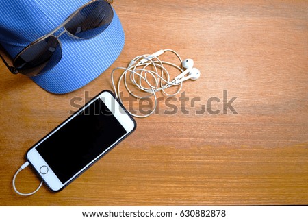 Denim cap, sunglasses, earphones and cellphones on wooden background.
